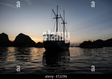 An Indonesian pinisi schooner sits at anchor near a set of remote limestone islands in Raja Ampat, Indonesia. Stock Photo