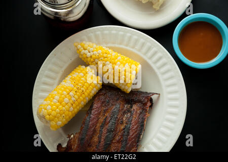 Pork ribs on a plate with corn on the cob, potato salad, iced tea, and barbeque sauce Stock Photo