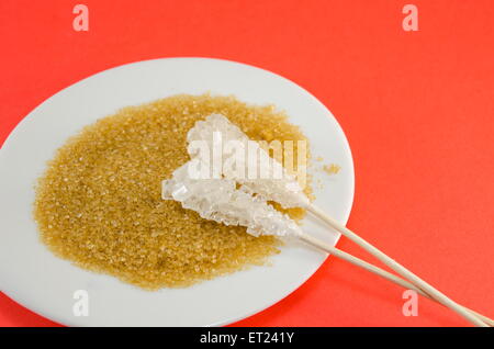 Two sugar sticks containing white and brown sugar in a black plate against a red background Stock Photo