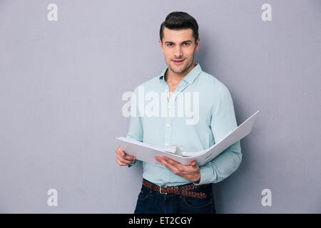 Young man standing with folder over gray background. Looking at camera Stock Photo