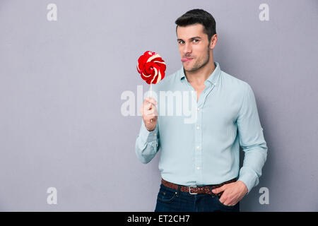 Funny young man holding lollipop over gray background and looking at camera Stock Photo