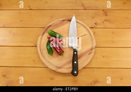 Red and green chillis with a sharp kitchen knife on a wooden chopping board Stock Photo