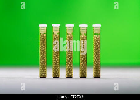 five small glass tubes with homeopathy globules, green background Stock Photo