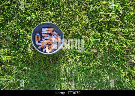Ashtray in grass. Ashtray with cigarette stubs in fresh green grass aerial view. Stock Photo
