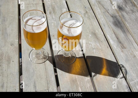 Two beers on rustic wooden table in Carlsberg logo glasses outdoors in sunshine. Stock Photo
