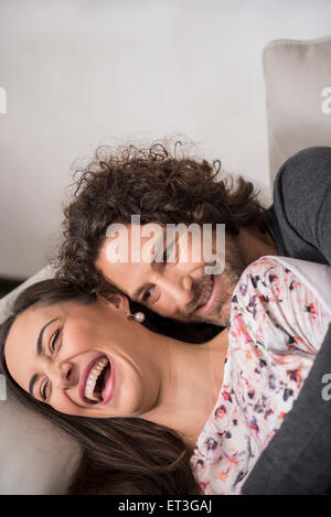 Mid adult couple lying on sofa and smiling, Munich, Bavaria, Germany