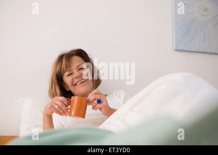 Senior woman in her bedroom drinking tea in the morning, Munich, Bavaria, Germany Stock Photo