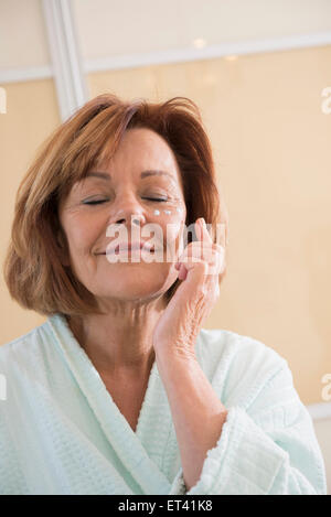 Senior woman applying moisturizer on her face, Munich, Bavaria, Germany Stock Photo