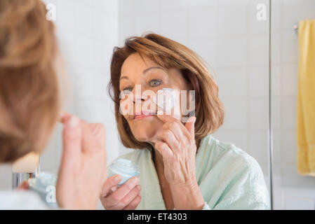Reflection of a senior woman applying moisturizer on her face in mirror, Munich, Bavaria, Germany Stock Photo