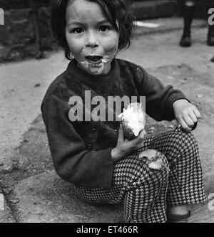 Slums, Benburb street area of Dublin, Republic of Ireland, 11th May 1968. Dublin slums controlled by the municipal authority, the Dublin Corporation, which has had to ignore standards of hygiene and sanitation. Pictured. Child enjoys a cream bun Stock Photo