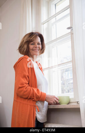 Side profile of senior woman smiling with having cup of tea at home, Munich, Bavaria, Germany