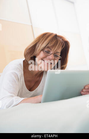 Senior woman lying on bed and using a digital tablet, Munich, Bavaria, Germany Stock Photo
