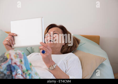 Senior woman lying on bed and using a digital tablet, Munich, Bavaria, Germany Stock Photo