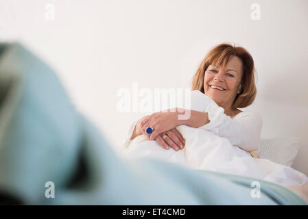 Portrait of senior woman sitting on bed and smiling, Munich, Bavaria, Germany