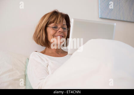 Senior woman sitting on bed and using a digital tablet, Munich, Bavaria, Germany Stock Photo
