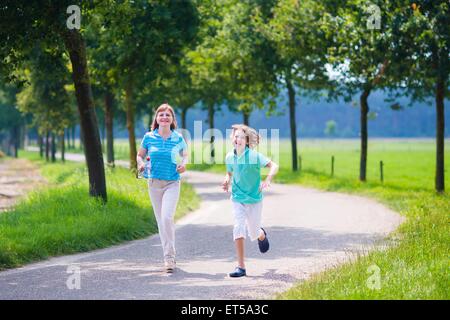 Happy healthy family, active young woman and a funny laughing boy, running together in a beautiful field, enjoying jogging sport Stock Photo