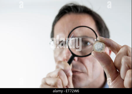 businessman examining one euro coin with magnifying glass, Bavaria, Germany Stock Photo