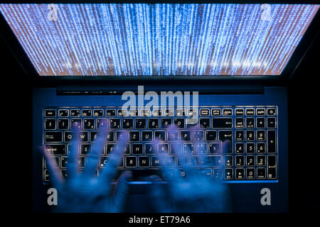 Hands are typing on a laptop computer in the dark with illuminated keyboard and mystic program code on screen Stock Photo