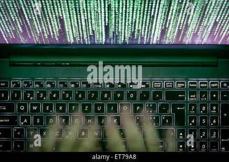 Hands are typing on a laptop computer in the dark with illuminated keyboard and mystic program code on screen Stock Photo
