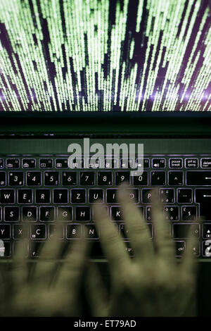 Hands are typing on a laptop computer in the dark with illuminated keyboard and mystic program code on screen Stock Photo