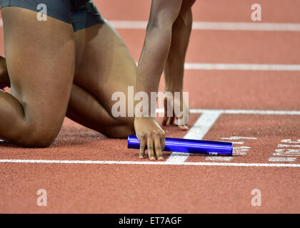 A female athlete (African ethnicity) holding a baton is getting set on the race track just before the start of a relay race Stock Photo