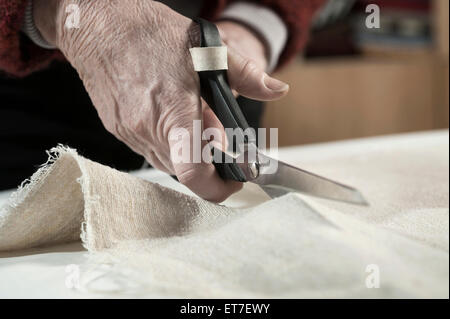 Senior female fashion designer cutting fabric with scissors in workshop Bavaria Germany Stock Photo