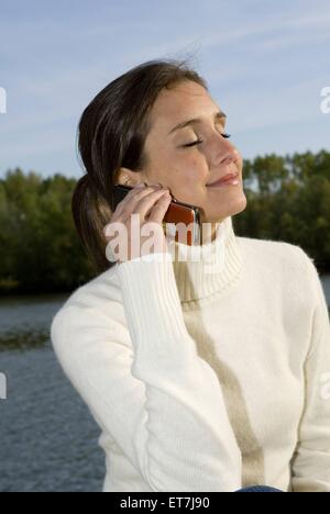 junge Frau am See telefoniert mit dem Handy, Oesterreich | young woman at a lake phoning with a mobile phone, Austria Stock Photo