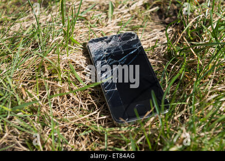 Close-up of smartphone with cracked screen lost in grassy field Bavaria Germany Stock Photo