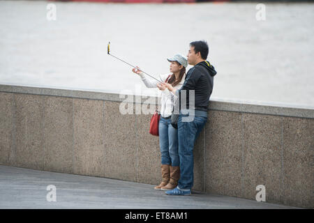 Japanese tourists taking selfie photographs using a selfie stick by the River Thames in London Stock Photo