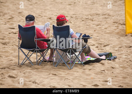 Couple sat in folding chairs, man reading newspaper, woman reading kindle, on Bournemouth Beach in June Credit:  Carolyn Jenkins/Alamy Live News Stock Photo