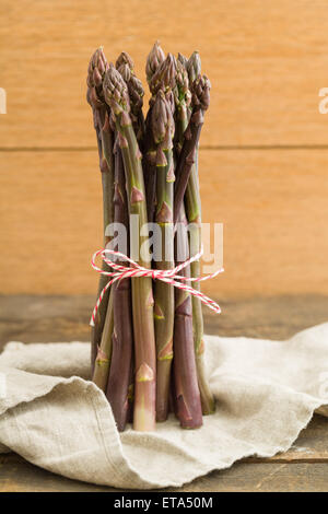 Bunch of fresh purple asparagus on wooden table with linen cloth Stock Photo