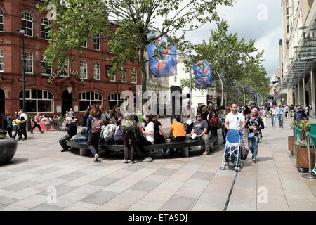 People sitting Muslim couple pushing child in pushchair on city street in Cardiff City Centre St Davids 2 shopping district pedestrian area in June sunshine Wales UK  Great Britain   KATHY DEWITT Stock Photo