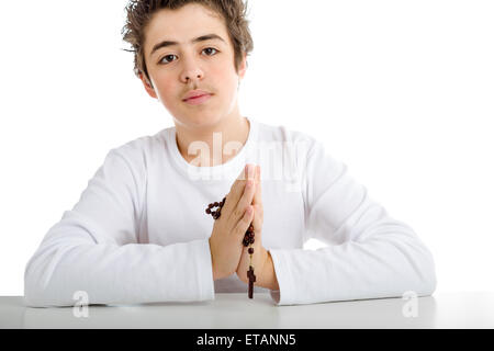 A Caucasian boy is praying and he holds Rosary beads with both hands Stock Photo