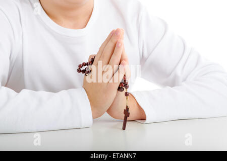 A Caucasian boy is praying and he holds Rosary beads with both hands Stock Photo