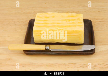 Block of butter with a knife in a dish on a wooden board Stock Photo