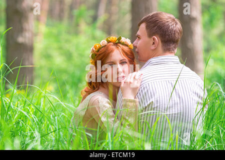 Beautiful lovers sitting on grass in forest, resting outdoors, gentle romantic feelings, happy wedding day, young new family Stock Photo