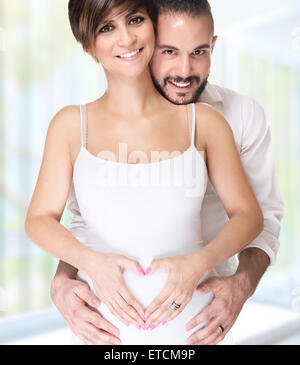 Portrait of beautiful happy couple holding hands in heart shape on the tummy, enjoying first pregnancy, happy young family Stock Photo