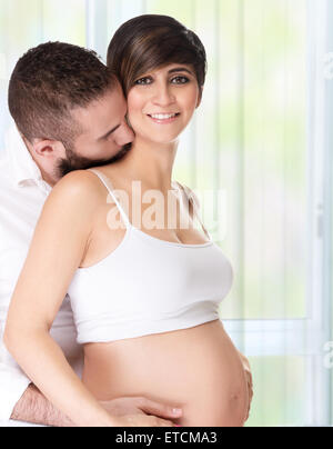 Portrait of loving couple at home, handsome man with passion kissing his beautiful pregnant wife, enjoying pregnancy Stock Photo