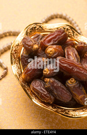 Arabic dates in a decorative golden bowl with prayer beads. Stock image. Stock Photo