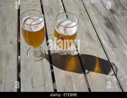 Two beers in Carlsberg logo glasses on rustic wooden table outdoors in sunshine on June 5, 2015 in Falkenberg, Sweden. Stock Photo