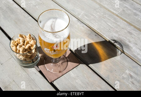 Two beers in Danish brand Carlsberg logo glasses on rustic wooden table with cashew nuts outdoors in sunshine. Stock Photo