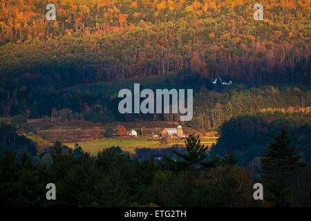 Early morning sunshine illuminates colored Autumn foliage surrounding a country farm in the hills of New Hampshire. Stock Photo
