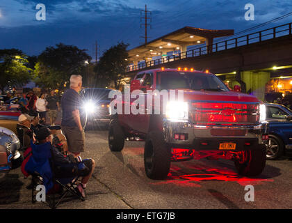 New York, USA. 12th June 2015. People watch as a custom GMC dually lifted diesel truck that is red underlit drives past to leave the Friday Night Car Show held at the Bellmore Long Island Railroad Station Parking Lot. Hundreds of classic, antique, and custom cars were on view at the free weekly show, sponsored by the Chamber of Commerce of the Bellmores. Stock Photo
