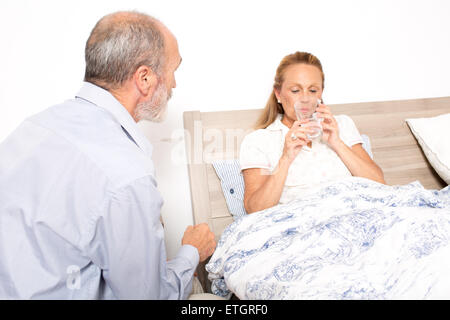 Elderly man is giving medication to an elderly woman which is in bed Stock Photo