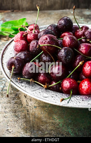 ripe large cherries in the iron bowl iron on the background in bright sunlight.The image is tinted.Selective focus Stock Photo