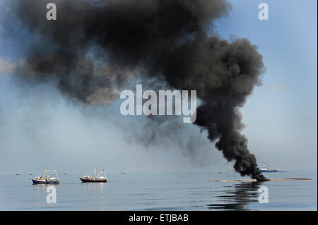 Dark clouds fill the sky as shrimp boats use a boom to gather crude oil during a controlled surface burn following the BP Deepwater Horizon oil spill disaster as efforts to contain and clean the millions of gallons of crew continue May 6, 2010 in the Gulf of Mexico. Stock Photo