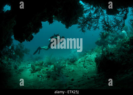 A diver explores the mouth of a deep cave in Raja Ampat, Indonesia. Stock Photo
