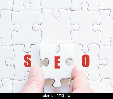Hand of a business man completing the puzzle with the last missing piece.Concept image of Business Acronym SEO as Search Engine Optimization Stock Photo