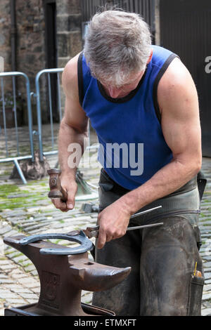 Farrier making a horseshoe and moulding it over an anvil while it was still red hot. Pollok Park, Glasgow, Scotland, UK Stock Photo