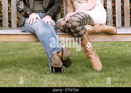 Low section of a couple wearing cowboy boots sitting on a bench Stock Photo